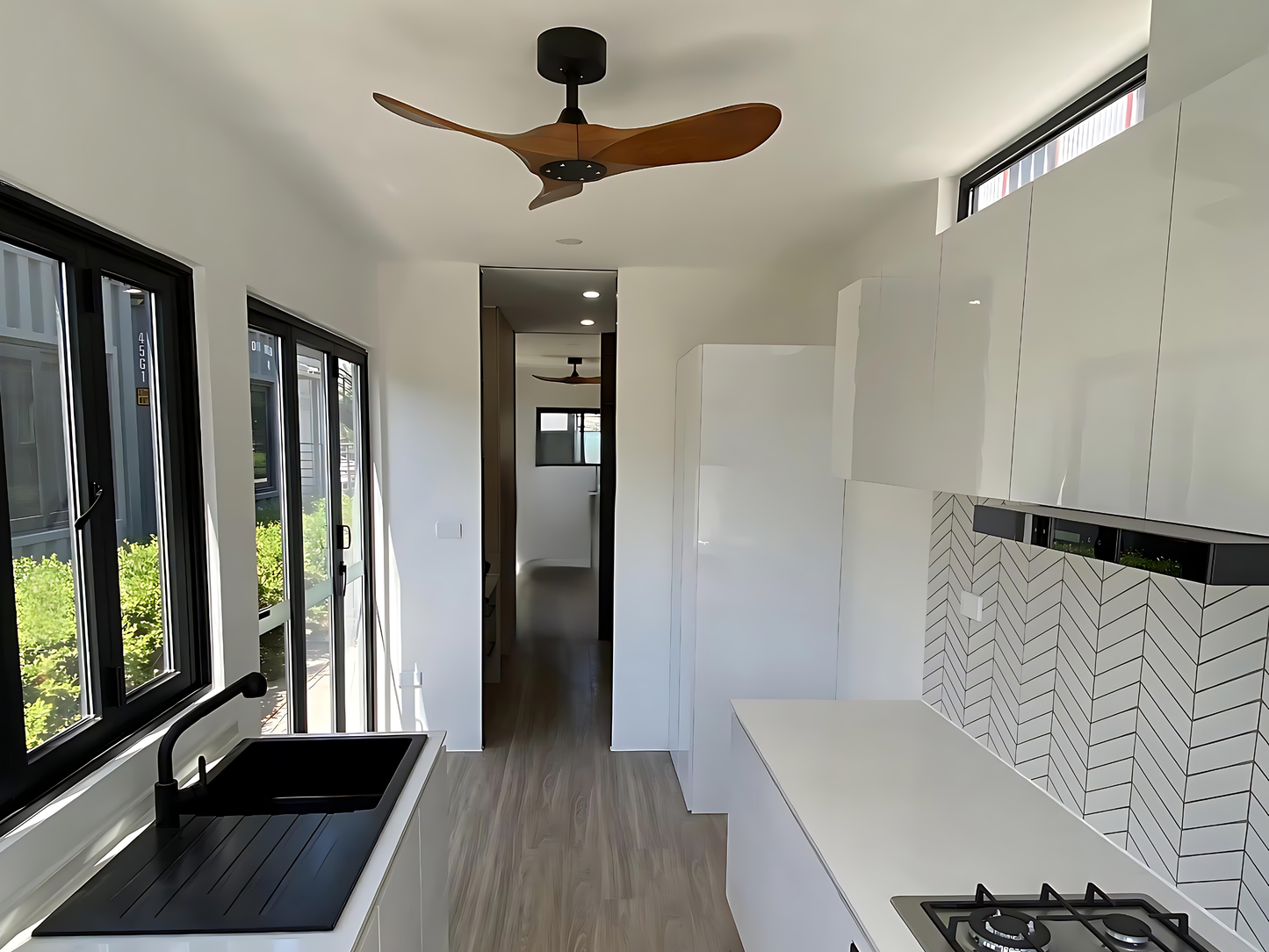 Modern kitchen interior with white cabinets, black countertop, and wooden ceiling fan.