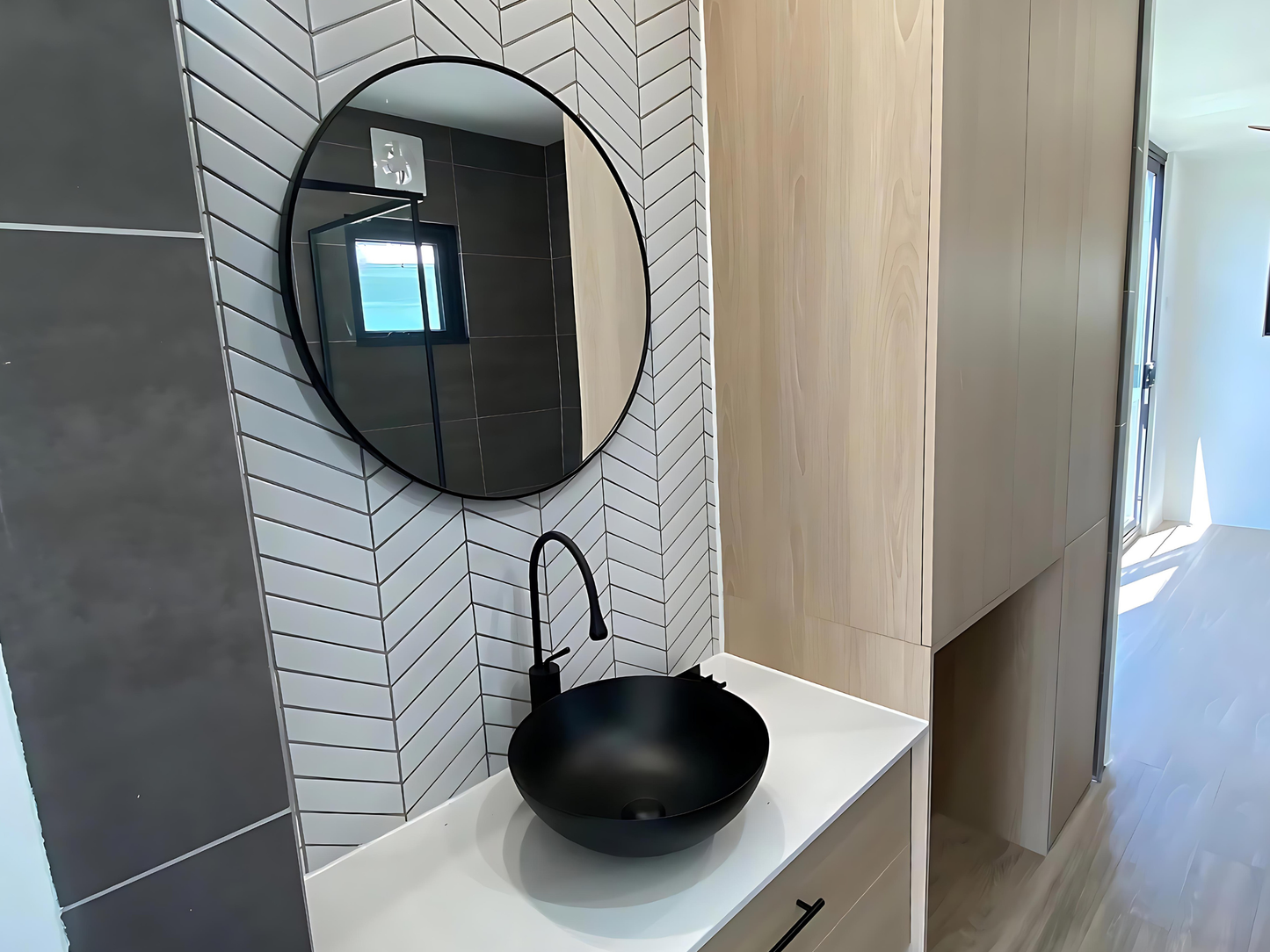 Bathroom with round mirror, black faucet, and tiled walls.