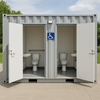 Container-based portable restroom facility with open doors showing toilets and sinks, featuring a wheelchair accessibility sign.