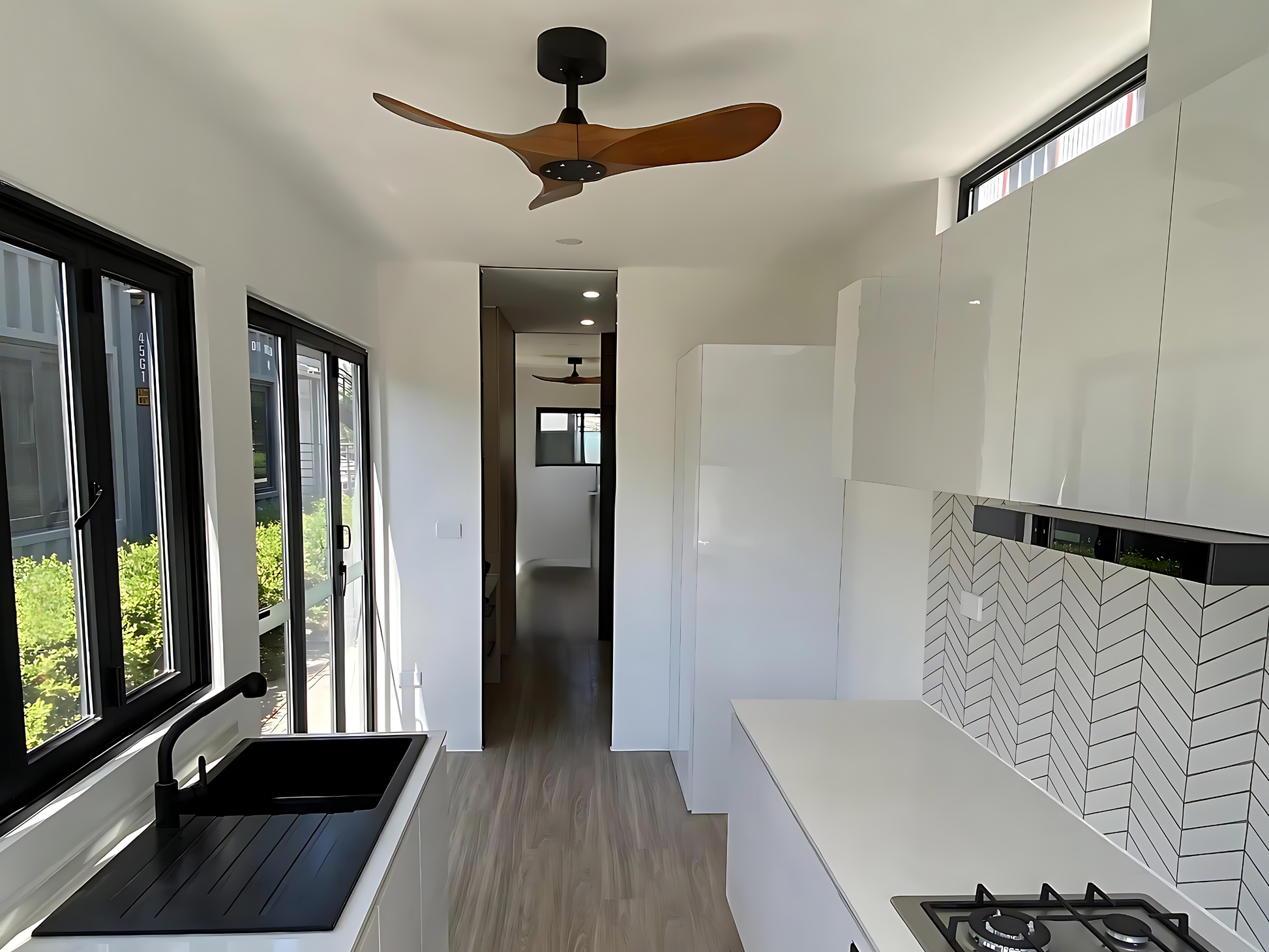 Modern kitchen interior with white cabinets, black countertop, and wooden ceiling fan.