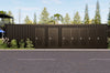 Row of dark brown containers restrooms with metal doors on a paved area with trees in the background.